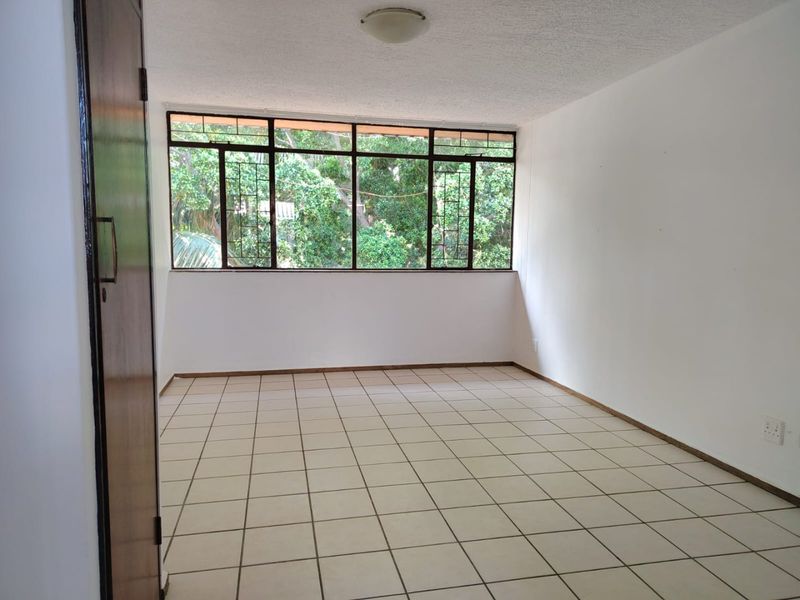 A spacious, empty bedroom featuring tiled flooring, a large window with security bars, and a built-in cupboard, offering a blank canvas for personalization.