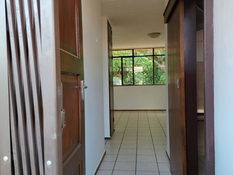 A bright, tiled hallway leading into an open living area with large windows, featuring wooden sliding doors and neutral wall finishes.