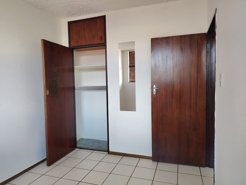 A vacant bedroom featuring tiled flooring, built-in cupboards with overhead storage, and dark wood-finish doors.