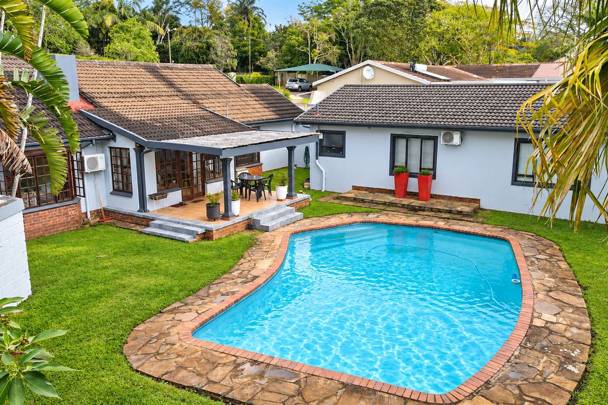 Rear exterior view featuring a swimming pool with stone surround, a covered patio area, and a well-maintained garden setting.