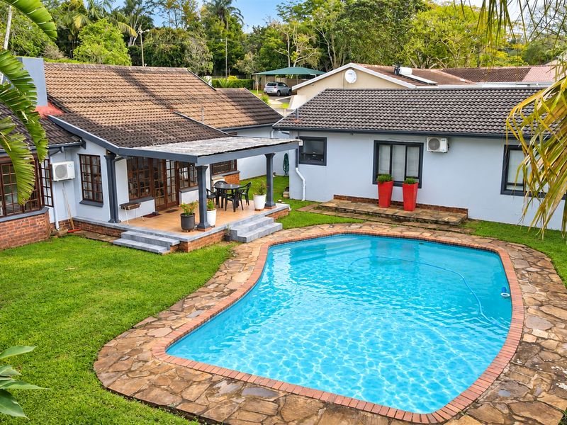 Rear exterior view featuring a swimming pool with stone surround, a covered patio area, and a well-maintained garden setting.
