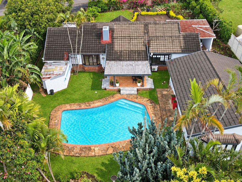 Aerial view of a residential property featuring a swimming pool, landscaped garden, and a covered patio area with a tiled roof.