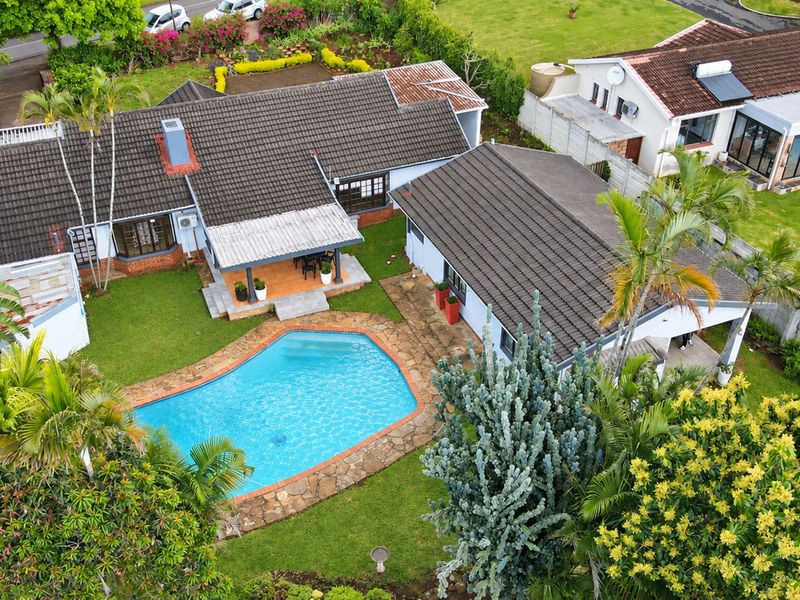 Aerial view of a residential property featuring a swimming pool, stone patio surround, and a tiled roof structure set within a landscaped garden.