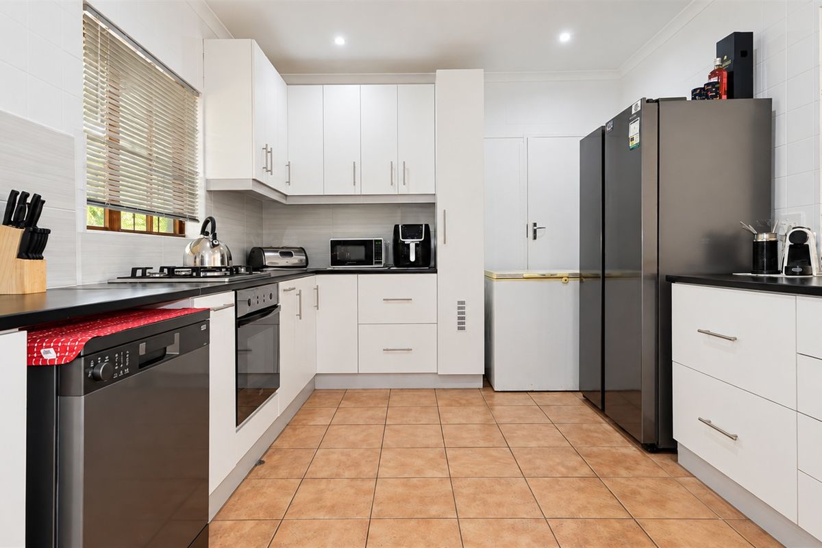 A functional kitchen featuring white cabinetry, dark countertops, tiled flooring, and integrated appliances, offering a clean and practical workspace.