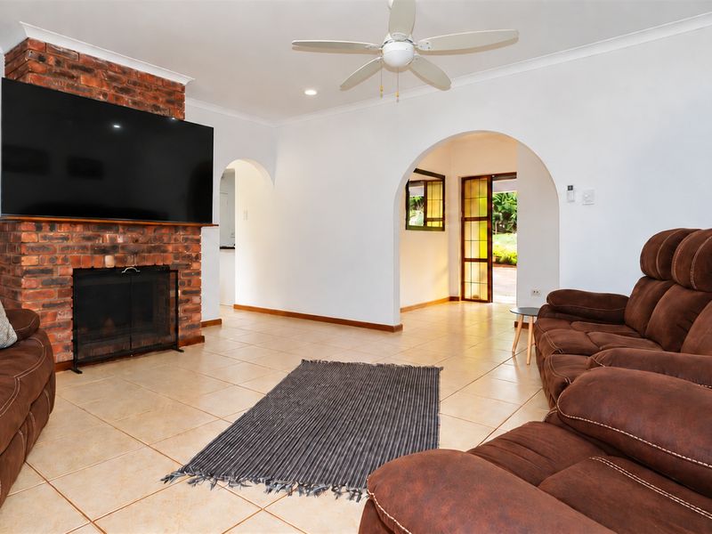 Spacious living room featuring a prominent brick fireplace, tiled flooring, and arched architectural details leading to adjacent areas.
