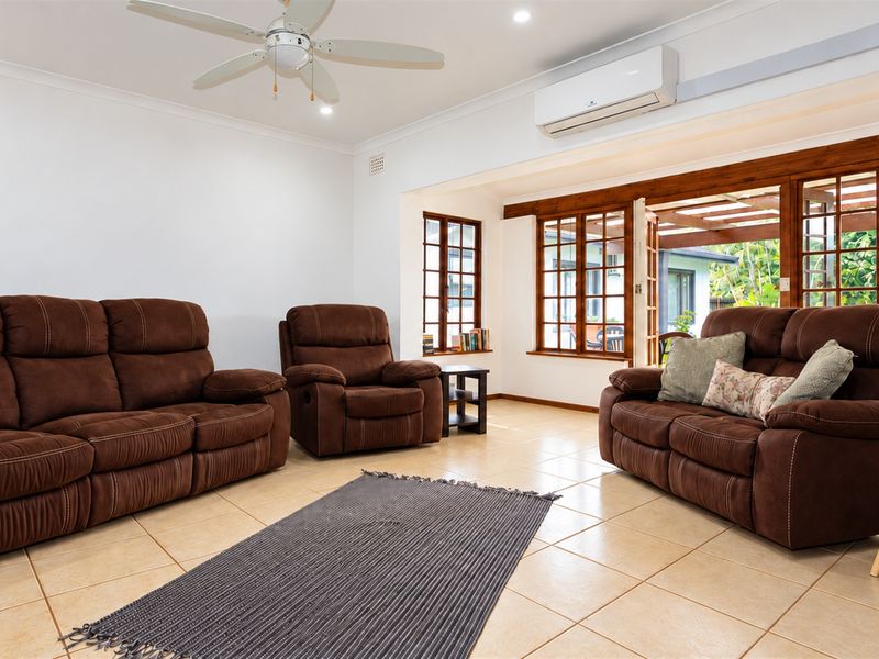 Spacious living room featuring tiled flooring, a ceiling fan, split system air conditioning, and timber-framed glass doors opening to an outdoor area.
