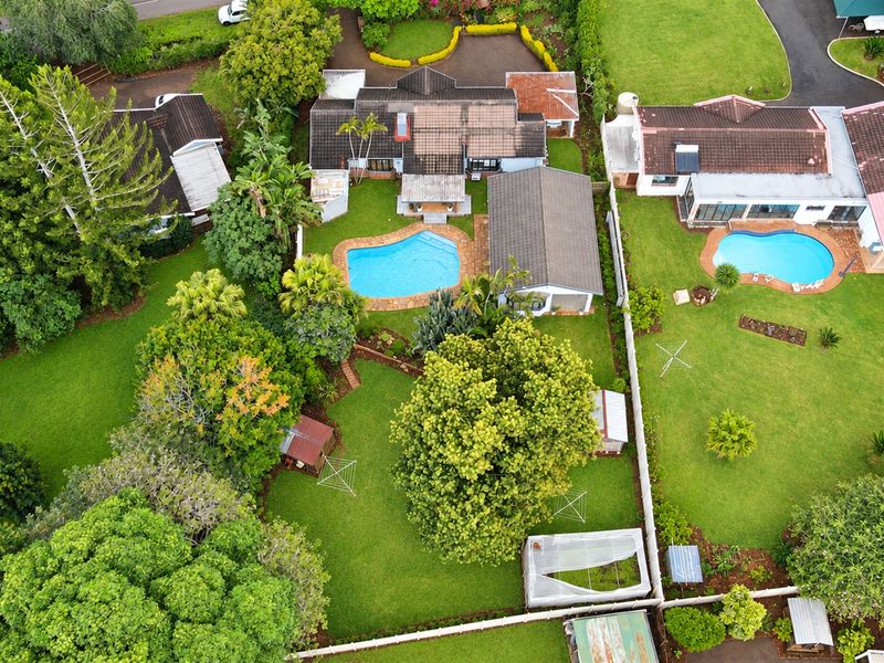 Aerial view of a residential property featuring a swimming pool, expansive garden, and tiled roof structures within a suburban neighborhood setting.