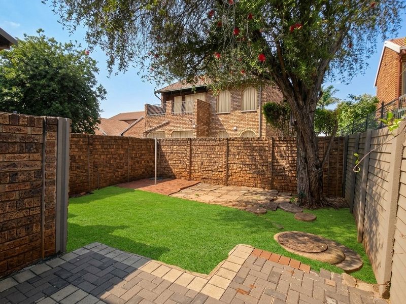 A private rear garden featuring a paved patio area, a well-maintained lawn, and brick boundary walls, providing a functional outdoor space.