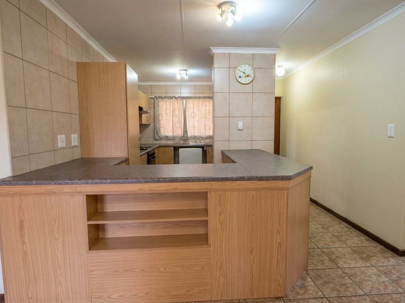 Open plan kitchen area featuring laminate cabinetry, tiled backsplash, and a breakfast bar, with adjacent tiled flooring and access to a bathroom.