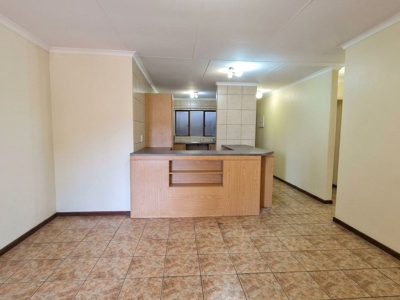 An open-plan living and kitchen area featuring tiled flooring, built-in cabinetry, and a breakfast counter, offering a functional and versatile layout.