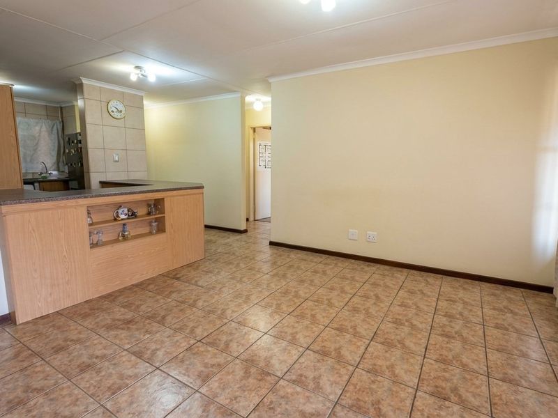 An open-plan living and kitchen area featuring tiled flooring, a breakfast bar, and neutral wall finishes, offering a versatile space for living and dining.