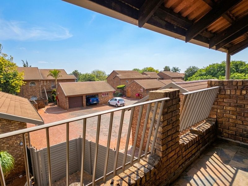 A covered balcony featuring a brick and metal balustrade with tiled flooring, overlooking the complex courtyard and garage area.