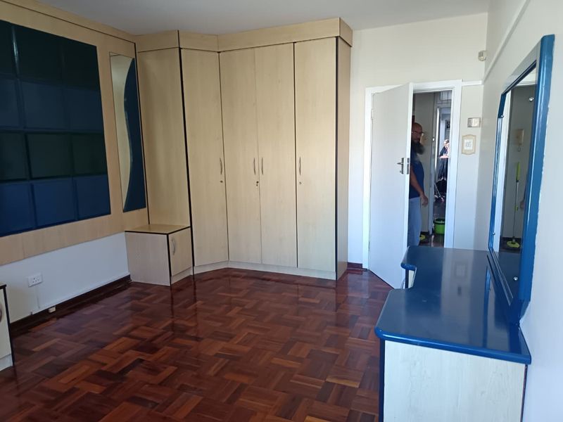 A bedroom featuring parquet flooring and extensive built-in cabinetry with an integrated vanity unit and mirror.