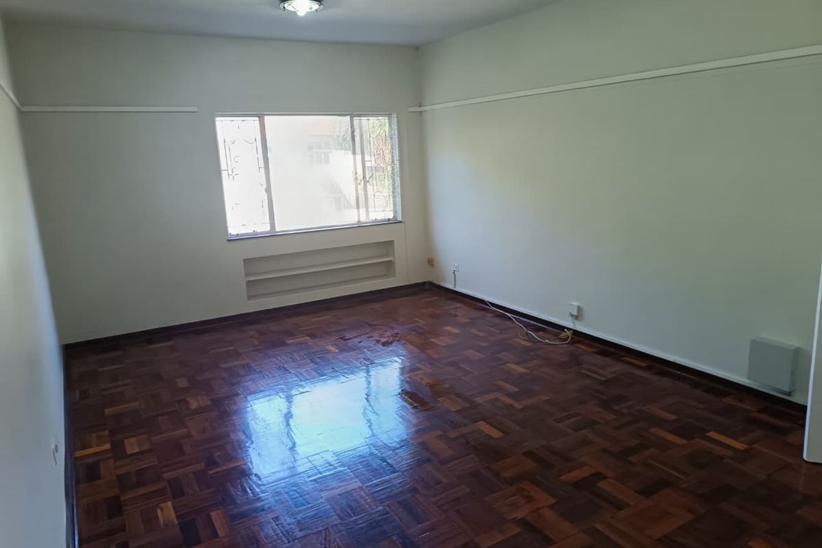 An empty living room featuring polished parquet flooring, a built-in wall niche, and a window with security bars.