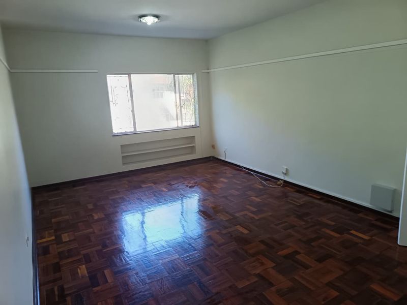 An empty living room featuring polished parquet flooring, a built-in wall niche, and a window with security bars.