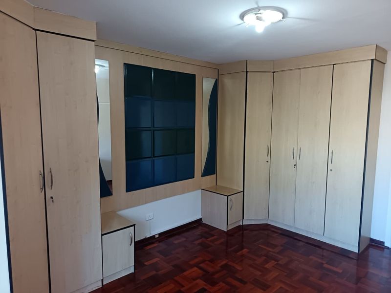 A spacious bedroom featuring extensive built-in wooden cupboards, integrated headboard with mirrored accents, and well-maintained parquet flooring.