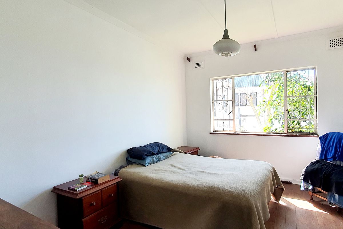 A bedroom featuring original timber flooring, a steel-framed window with security bars, and a central pendant light fixture.
