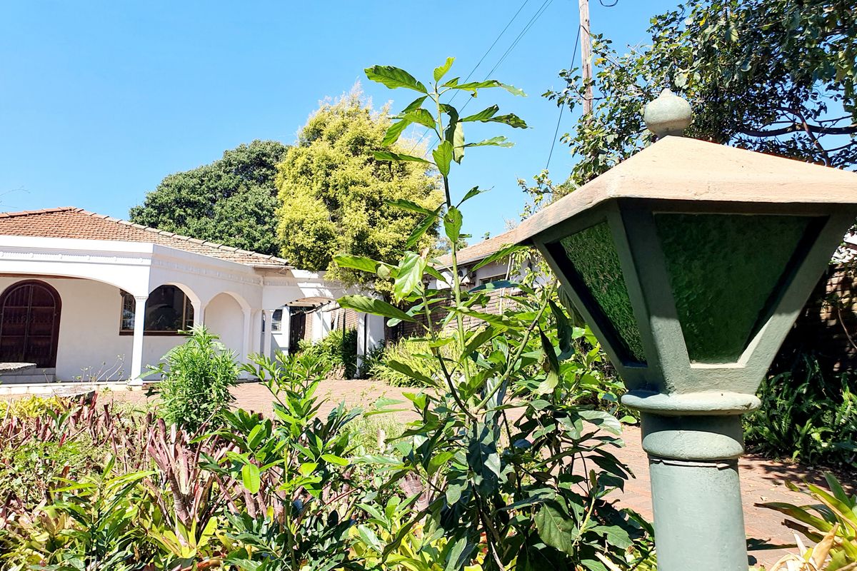 A view of the rear garden area featuring a paved courtyard, an arched veranda, and a classic garden lamp post.