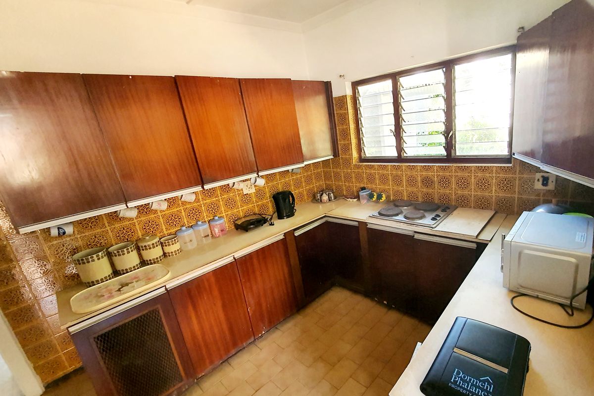 A dated kitchen featuring original wooden cabinetry, laminate countertops, and a patterned tiled backsplash, offering significant potential for a modern renovation.