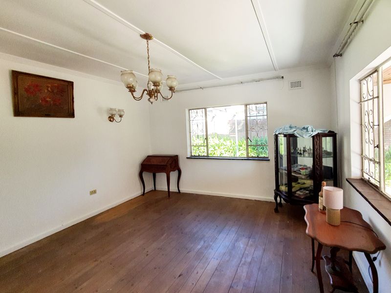 A living room featuring original timber flooring, large windows with security bars, and classic light fixtures, offering a blank canvas for renovation.