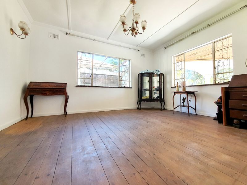 Spacious living room featuring original timber flooring, large windows with security bars, and classic ceiling and wall lighting fixtures.