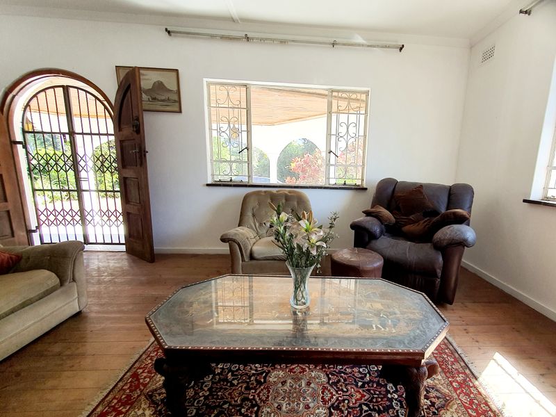 A living room featuring hardwood flooring, an arched security gate entrance, and windows fitted with security bars.