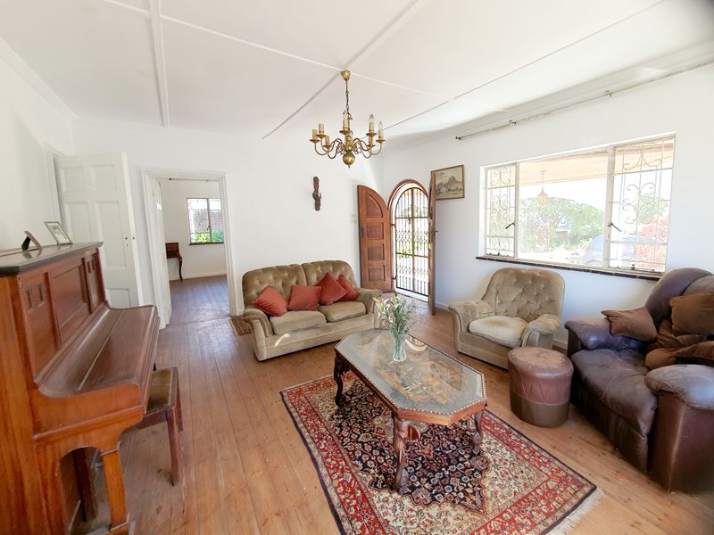 A spacious living room featuring original timber flooring, a classic chandelier, and large windows with security bars, offering a bright and traditional atmosphere.
