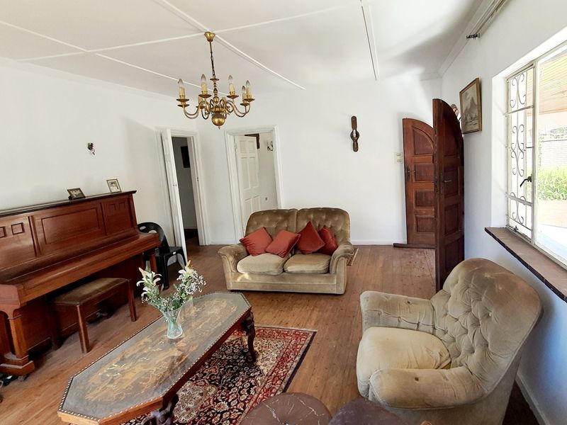 A spacious living room featuring original hardwood flooring, classic timber doors, and a traditional chandelier, offering a blank canvas for modern renovation.