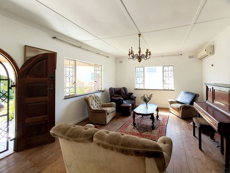 A spacious living room featuring original hardwood flooring, an arched timber entrance door, security-barred windows, and a wall-mounted air conditioning unit.