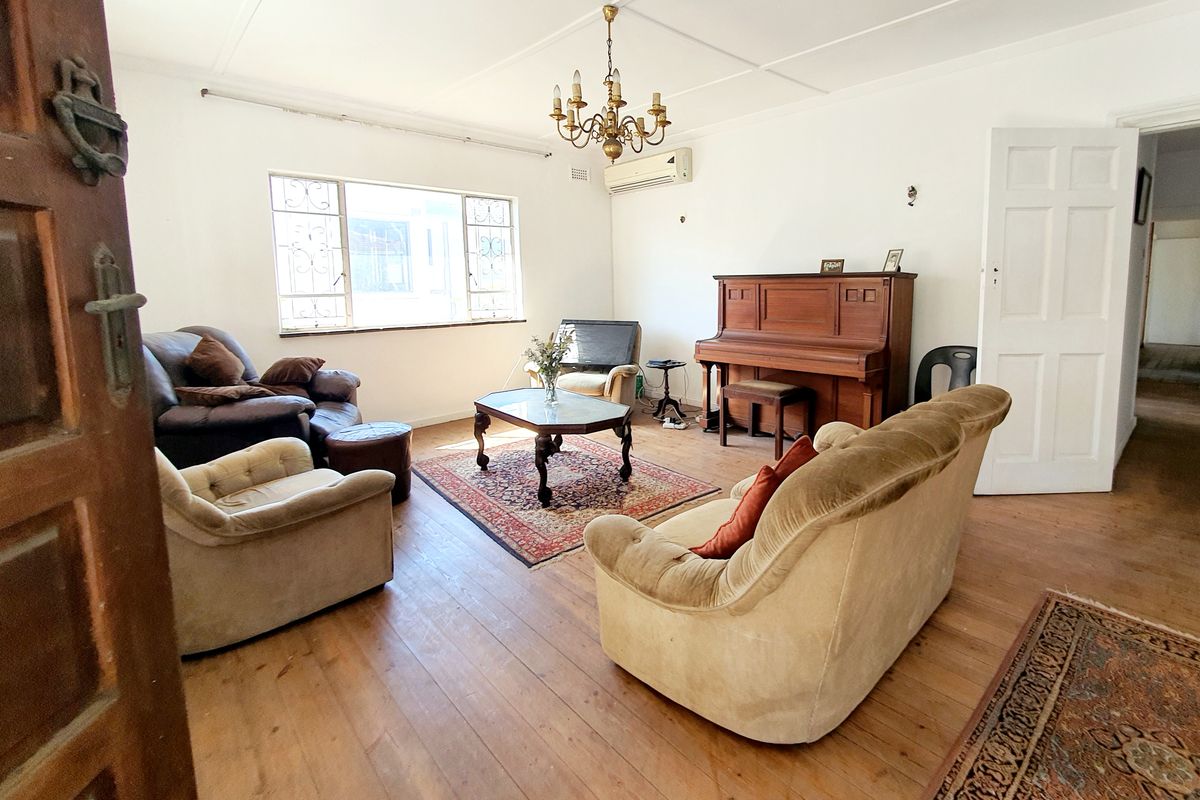 Spacious living room featuring original timber flooring, a split-system air conditioner, and classic chandelier lighting, offering a versatile layout for comfortable family living.