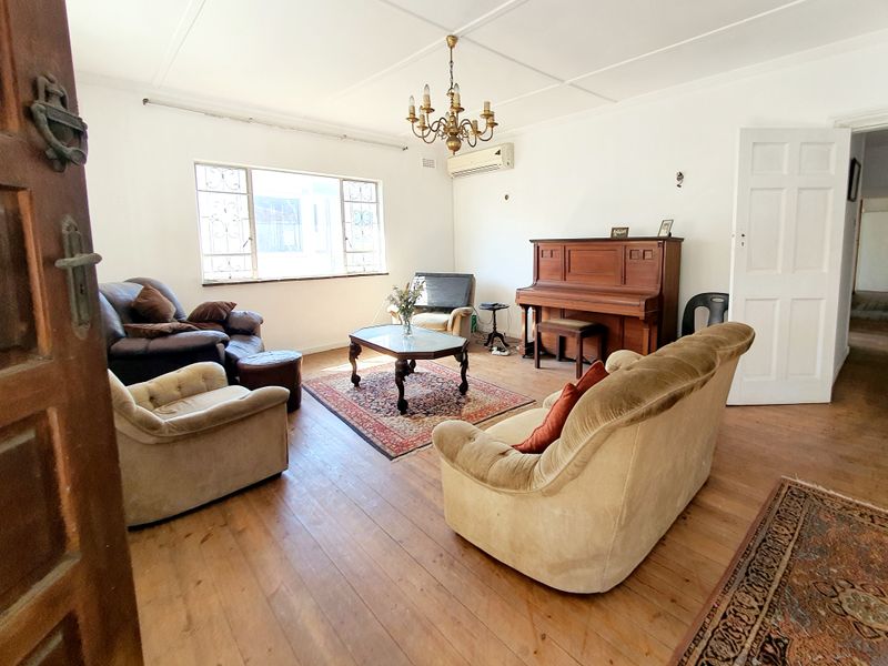 Spacious living room featuring original timber flooring, a split-system air conditioner, and classic chandelier lighting, offering a versatile layout for comfortable family living.