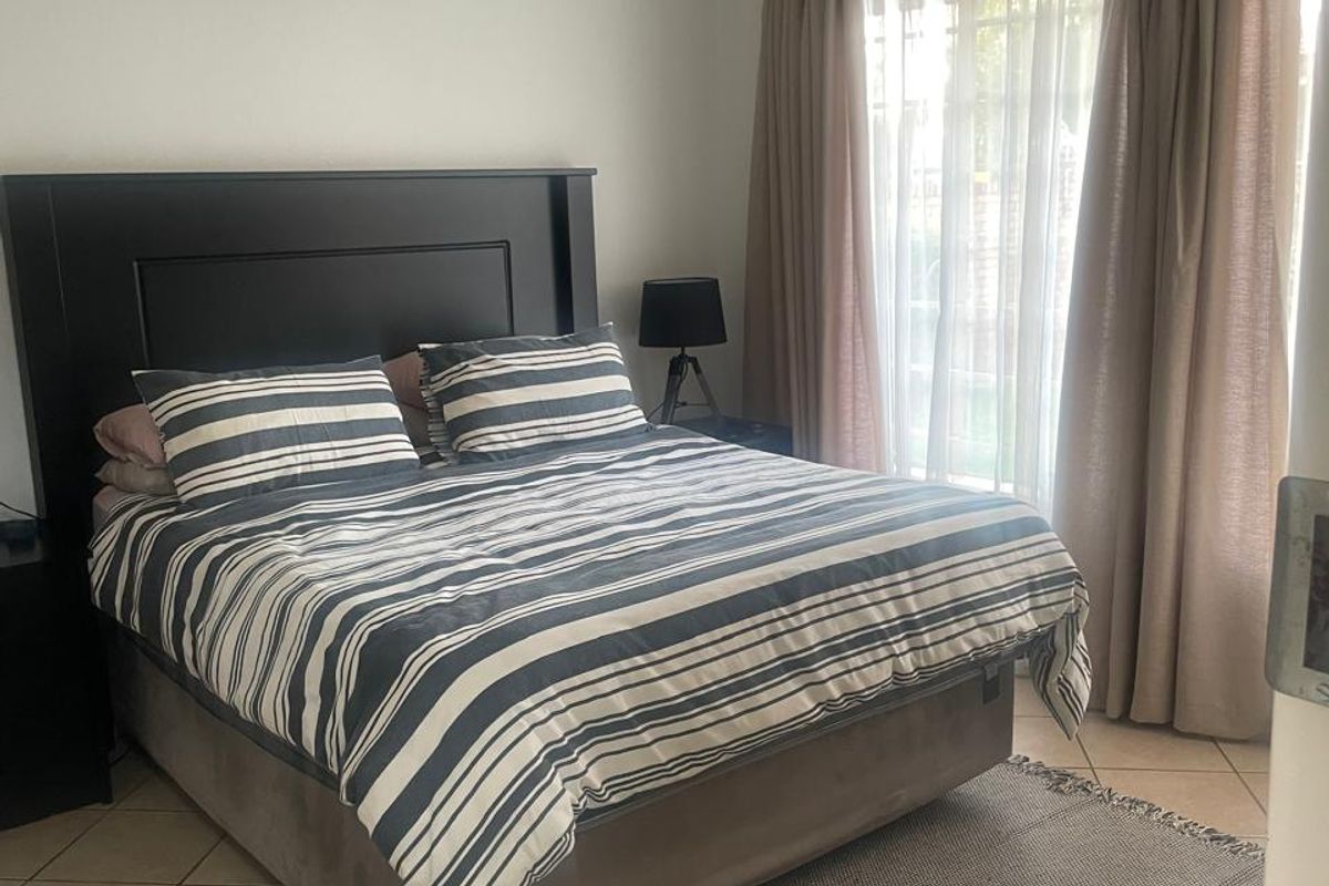 A bedroom featuring ceramic tiled flooring, a wall-mounted split-system air conditioner, and large windows with curtain treatments.