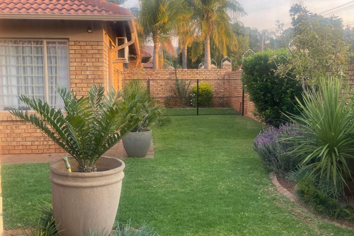 A well-maintained rear garden featuring a brick townhouse facade, tiled roof, paved patio area, and established landscaping with a secure boundary wall.