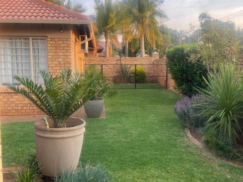 A well-maintained rear garden featuring a brick townhouse facade, tiled roof, paved patio area, and established landscaping with a secure boundary wall.