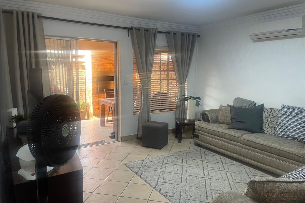 A comfortable living room featuring tiled floors, a wall-mounted air conditioner, and a sliding door providing direct access to an outdoor patio area.