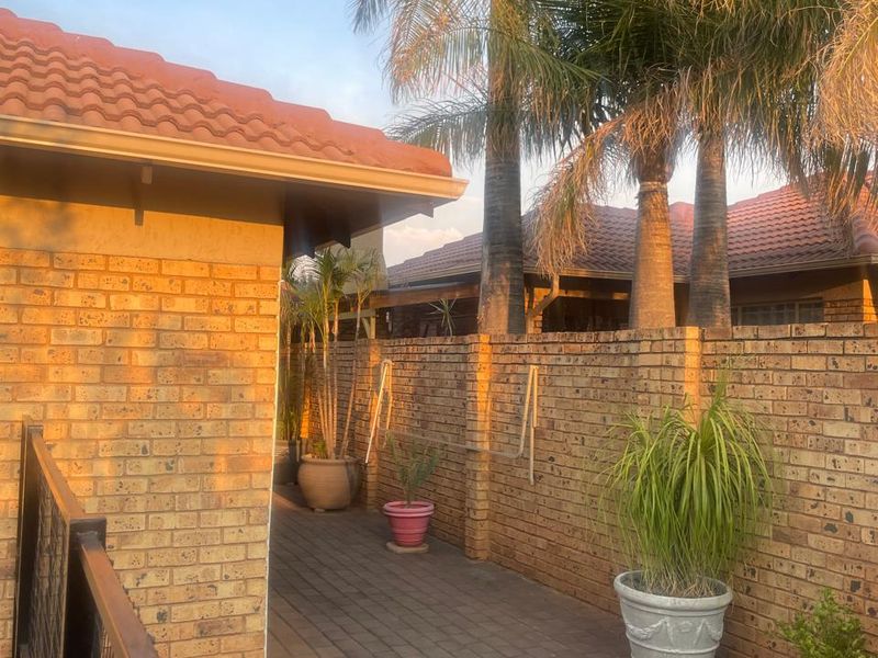 A side exterior view of the townhouse featuring a brick facade, paved walkway, and established palm trees in a private garden setting.