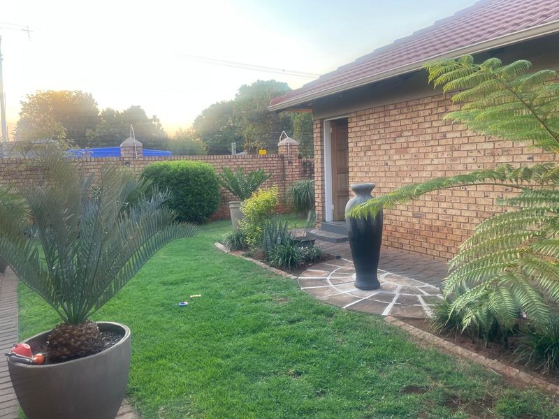 A well-maintained rear garden featuring a face brick exterior, paved patio area, and established landscaping with a lawn and perimeter boundary wall.