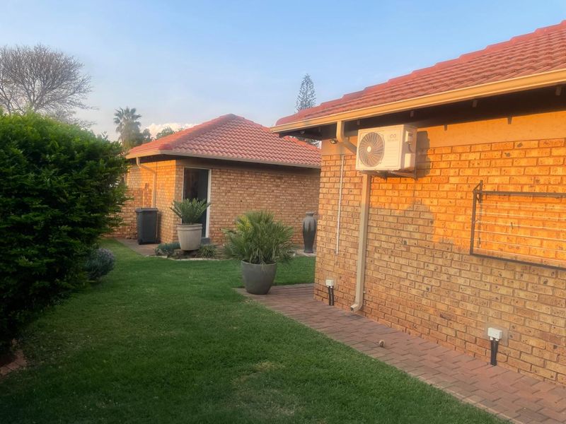 Rear view of the townhouse featuring face brick exterior, tiled roofing, a paved walkway, and a well-maintained garden area.