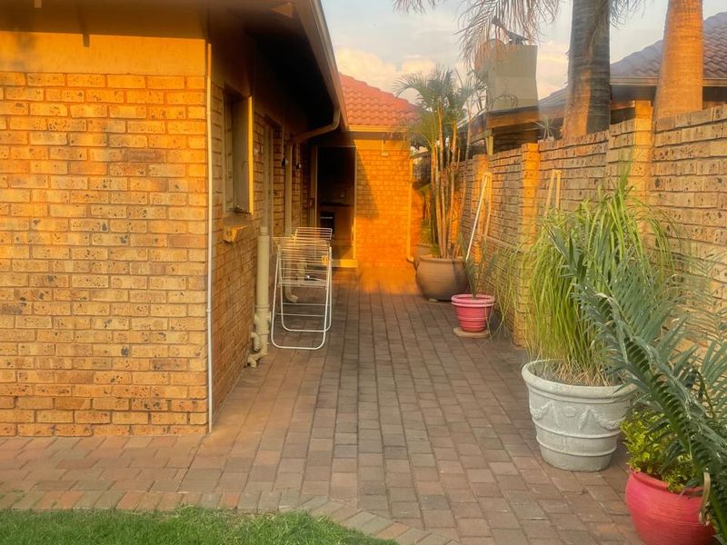 A side exterior view of the townhouse featuring face brick walls, a tiled roof, and a paved walkway leading to the rear area.
