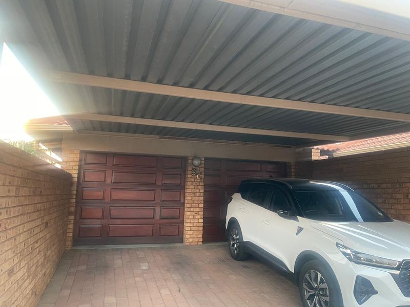 A double garage with wooden doors and an attached carport, featuring brick wall construction and paved driveway area.