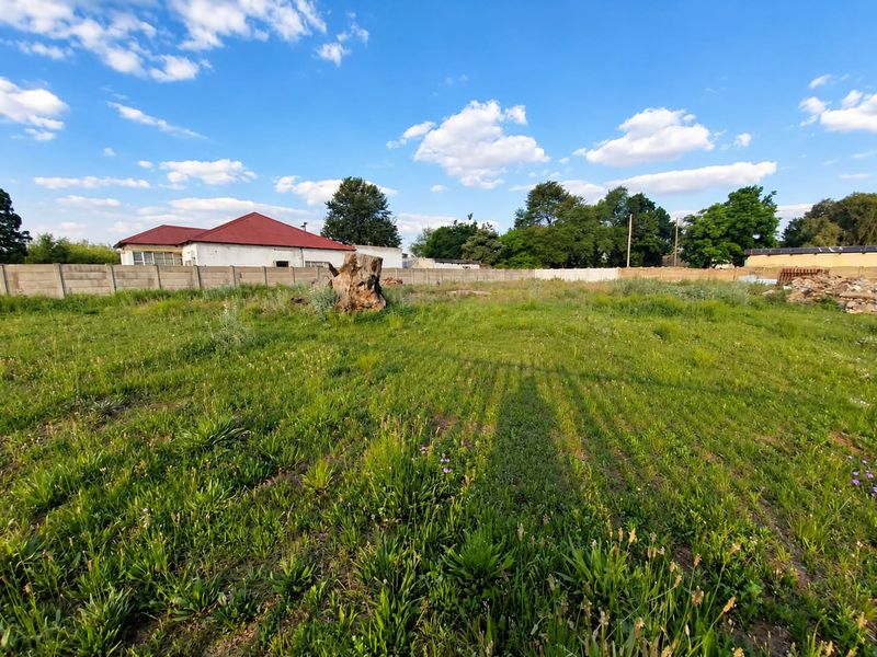 A vacant residential plot featuring a precast concrete boundary wall and natural grass coverage, suitable for future development.