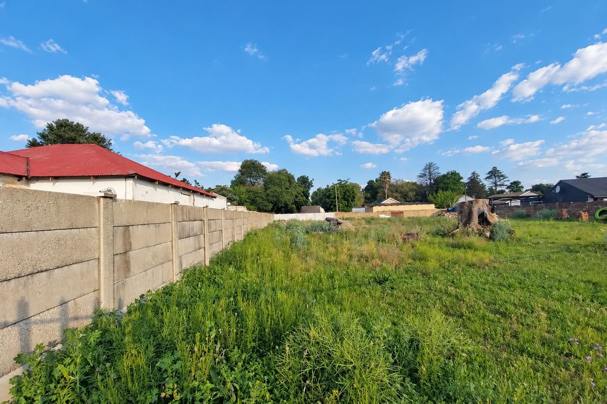 A view of a vacant residential plot featuring a precast concrete boundary wall and natural vegetation.