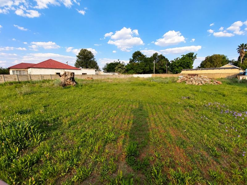 A vacant residential plot featuring a precast concrete boundary wall, natural grass cover, and some site debris, offering a blank canvas for development.