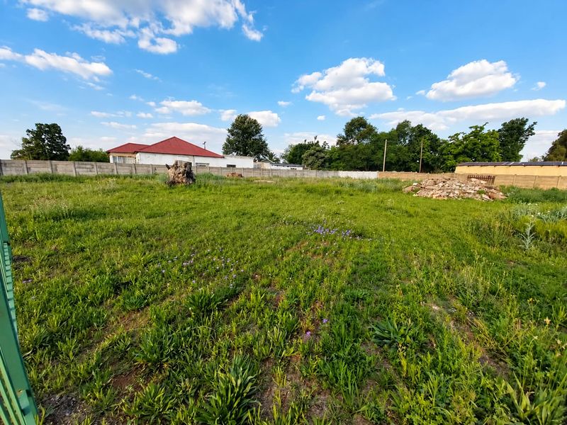 A vacant residential plot featuring a perimeter precast concrete wall, open grassed area, and existing boundary fencing.