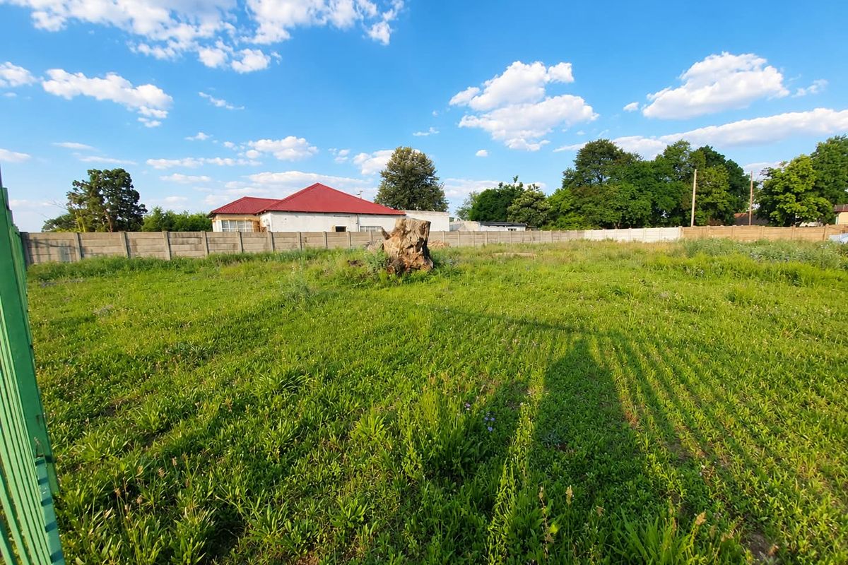 A vacant residential plot featuring a level grassed area, enclosed by a precast concrete boundary wall and metal gate.