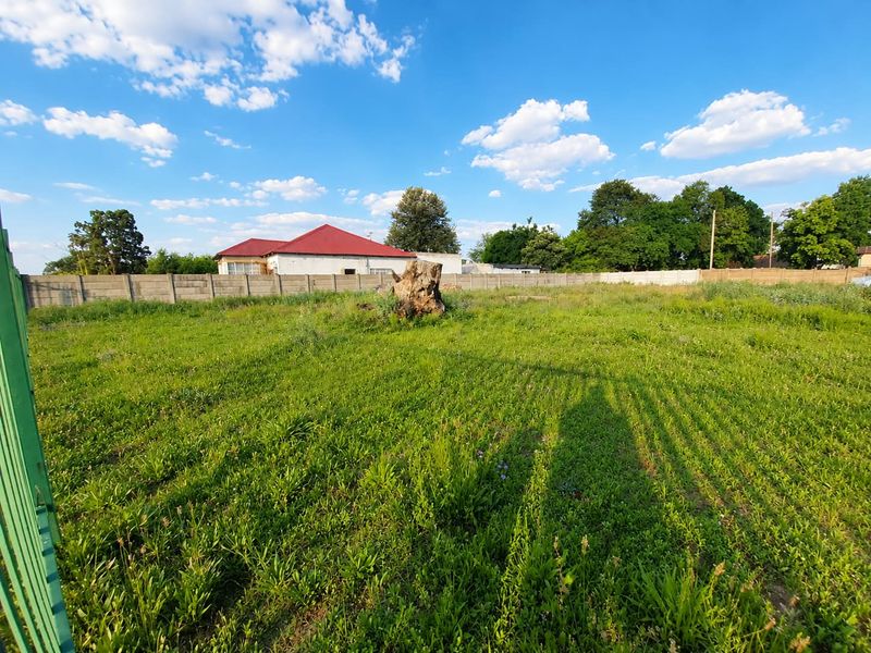 A vacant residential plot featuring a level grassed area, enclosed by a precast concrete boundary wall and metal gate.