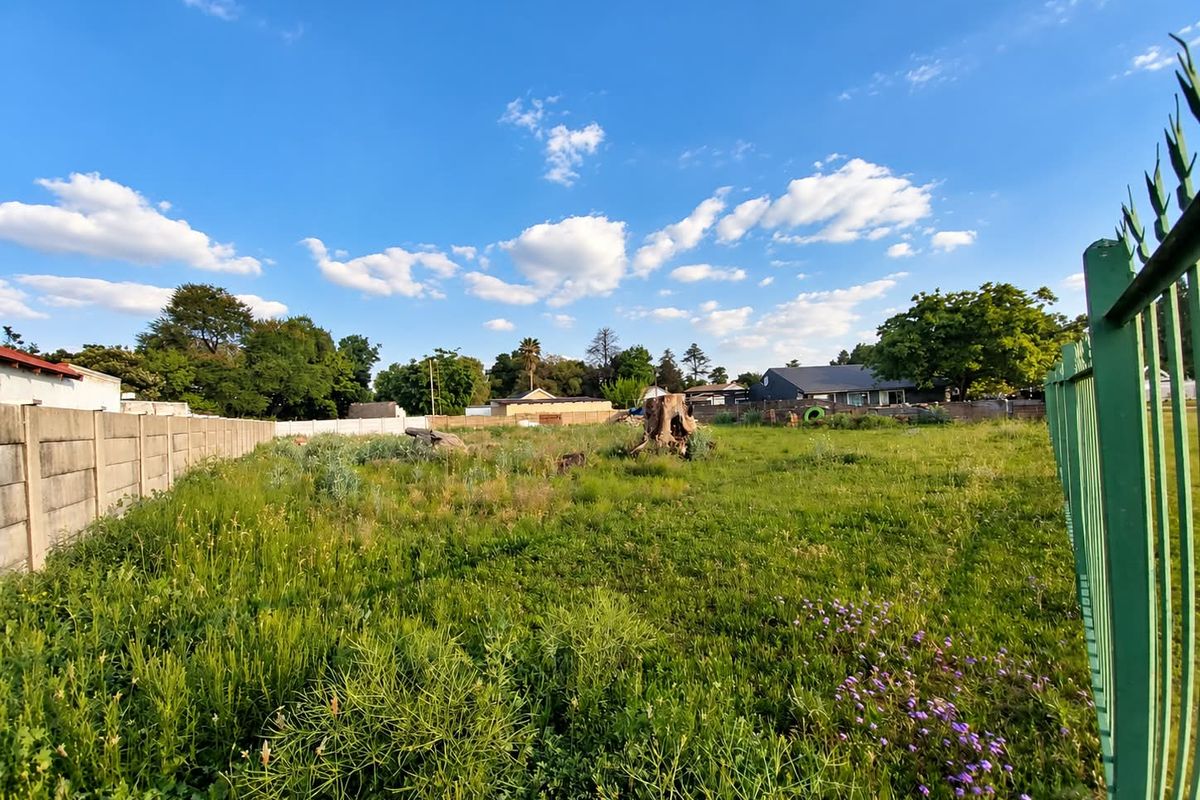 A vacant residential plot featuring established boundary walls and metal fencing, currently covered in overgrown grass and vegetation.