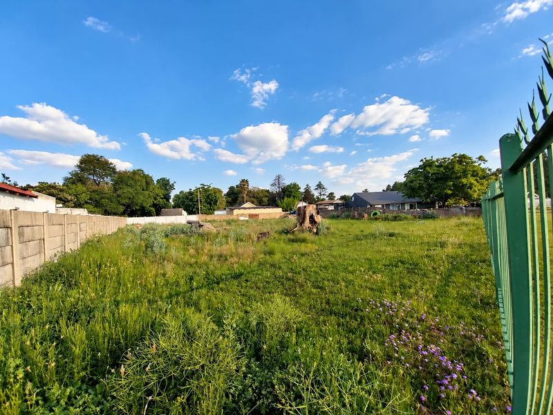 A vacant residential plot featuring established boundary walls and metal fencing, currently covered in overgrown grass and vegetation.