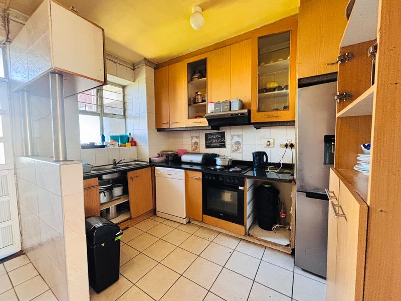 A functional kitchen featuring wooden cabinetry, granite countertops, built-in oven, and tiled flooring, offering potential for modernization and aesthetic updates.