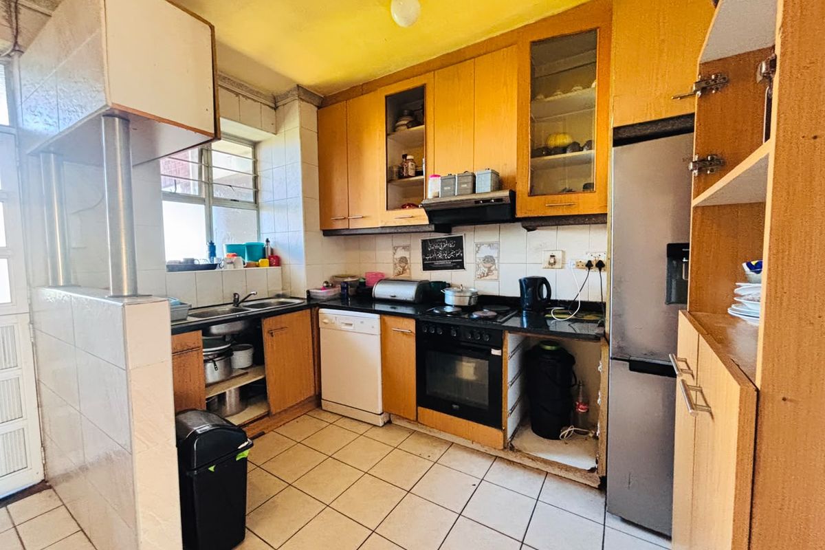 A functional kitchen featuring wooden cabinetry, granite countertops, built-in oven, and tiled flooring, offering potential for modernization and aesthetic updates.